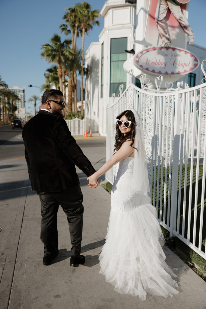bride and groom walking on sidewalk outside of the world famous little white wedding chapel in las vegas